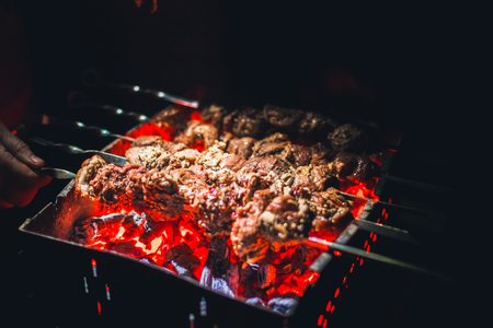 Grilled kebab cooking on metal skewers (grill). Roasted meat cooked at barbecue with smoke. Close up BBQ fresh pork meat chop slices. Traditional eastern dish, shish kebab.の写真素材