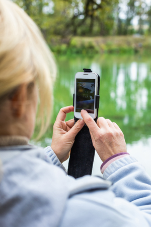 A blonde woman using a phone takes a photo of a beautiful landscape.の写真素材