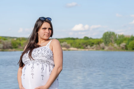 Pregnant woman in a white dress near the waterの写真素材