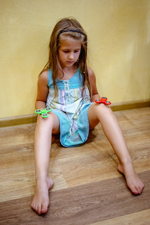 Little girl playing with green and red fidget spinners to relieve stress at homeの写真素材