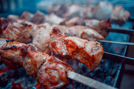 Grilled kebab cooking on metal skewers (grill). Roasted meat cooked at barbecue with smoke. Close up BBQ fresh pork meat chop slices. Traditional eastern dish, shish kebab. Grill on charcoal and flame, picnic, street food. Toned, style, classic photo.の写真素材