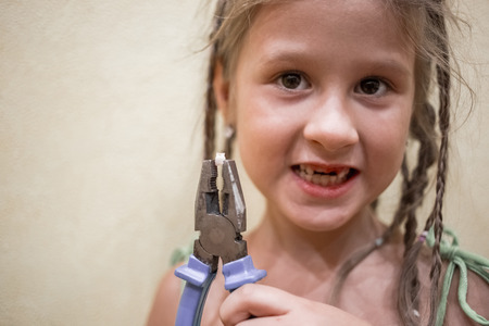 A little girl and pliers with a milk tooth. Tearing out the teeth at home.の写真素材
