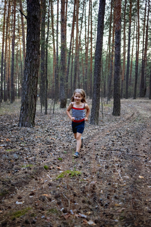Little girl run in the pine forest in summer.の写真素材