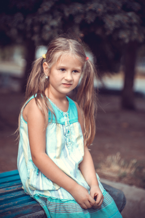 Portrait of a little girl in the park on a bench in the summer timeの写真素材