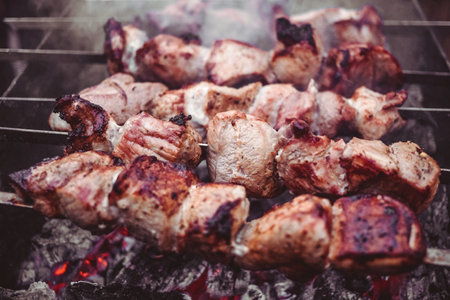 Grilled kebab cooking on metal skewers (grill). Roasted meat cooked at barbecue with smoke. Close up...