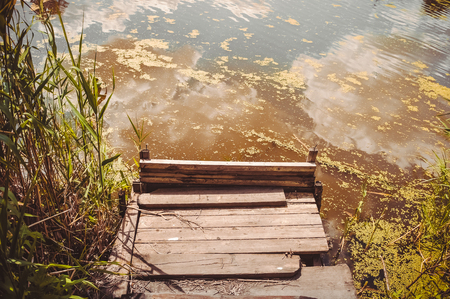 Wooden platform for fishing on the river in summer. Duckweed, reflection of trees and sky in the water.の写真素材