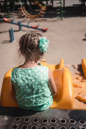 Alone little girl on the playground in summer. Back view.の写真素材