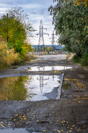 Old road with puddles in the industrial area in autumnの写真素材