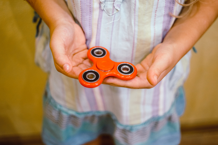 Little girl playing with red fidget spinner toy to relieve stress at homeの写真素材
