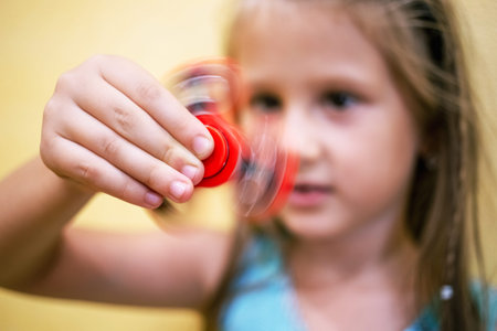 Little girl playing with red fidget spinner toy to relieve stress at homeの写真素材