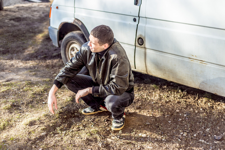 A young guy of criminal appearance in a black leather jacket stands near an old white van.の写真素材