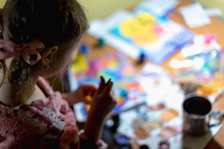 Cute little girl painting with paintbrush and colorful paints in home interior.の写真素材