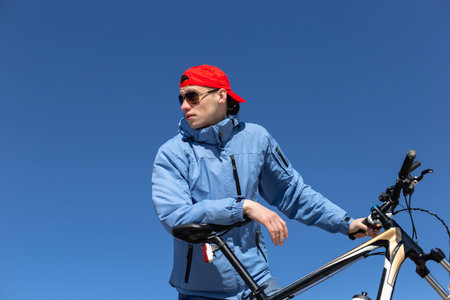 Young guy with bicycle on blue sky background.
