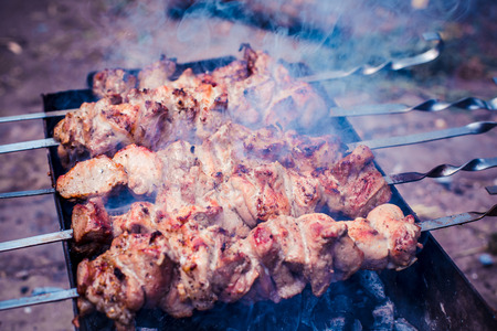 Grilled kebab cooking on metal skewers (grill). Roasted meat cooked at barbecue with smoke. Close up BBQ fresh pork meat chop slices. Traditional eastern dish, shish kebab.の写真素材