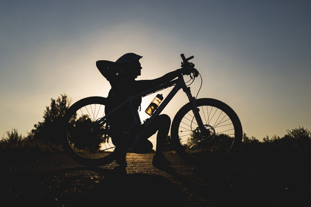 Silhouette of a girl with a bicycle at sunset in the summer.の写真素材