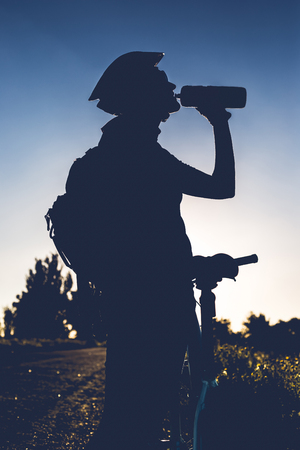 Silhouette of drinking water girl with a bicycle at sunset.の写真素材