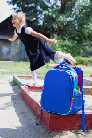 Back to school concept. A school backpack in the foreground and a junior schoolgirl on the playground in the background. Accent photos on a school backpack.の写真素材