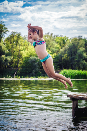 Little cute girl jumping off the dock into a beautiful river at sunset.の写真素材