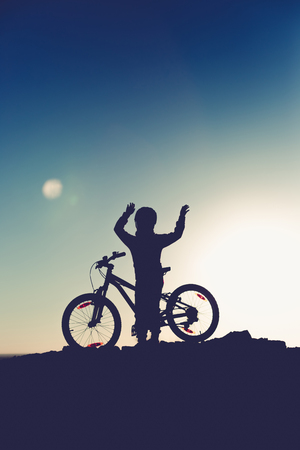 Silhouette of a little girl with a bicycle at sunset.の写真素材