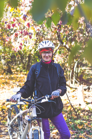 Cute young woman on a bicycle in the autumn forest.の写真素材
