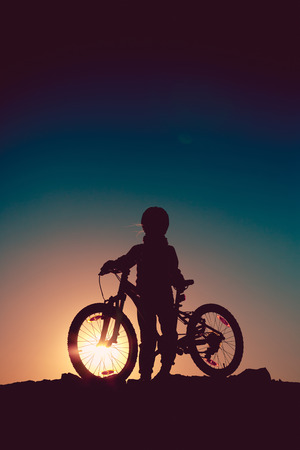 Silhouette of a little girl with a bicycle at sunset.の写真素材