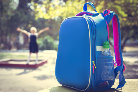 Back to school concept. A school backpack in the foreground and a junior schoolgirl on the playground in the background. Accent photos on a school backpack.の写真素材