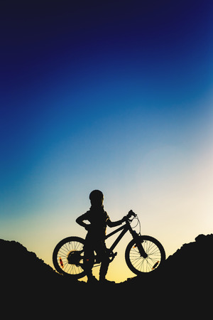 Silhouette of a little girl with a bicycle at sunset.の写真素材