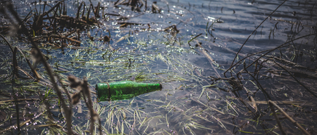 Green beer bottle in the pond. The concept of environmental pollutionの写真素材