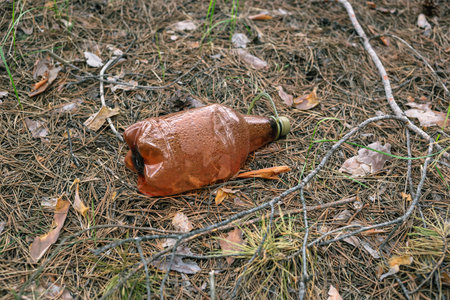 Brown plastic bottle on the ground in a pine forest. Environmental Pollution Concept
