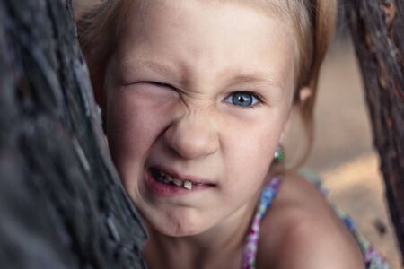 A little girl near a pine tree shows a wobbly baby tooth in her mouthの写真素材