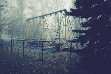 Swing boats in an old abandoned park on a foggy autumn morning.の写真素材