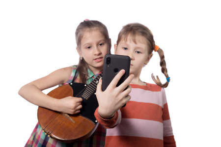 Two cute little girls take selfie on a smartphone. Studio photo on a white background.