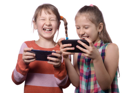 Two cute little girls posing with mobile phones. Girls play on mobile phones. Studio photo isolated...