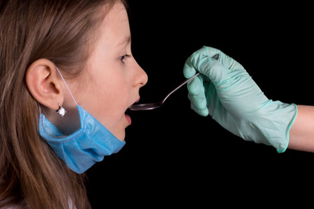 Cute little girl is taking medicine from a doctor. On the girl's face there is a mask to protect...