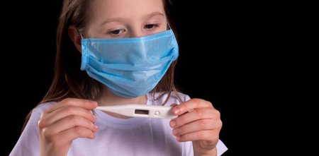 Cute little girl with a thermometer. A mask on her face to protect against the Covid19. Studio photo...