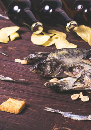 Dried fish, perch, bleak, chips, crackers, nuts and three brown glass bottles of beer on a wooden background. Studio photo.の写真素材