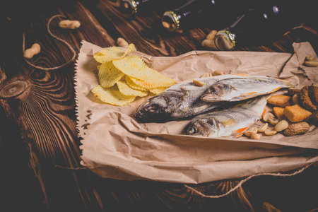 Brown glass bottles of beer and dried fish with chips, nuts, crackers on paper on a wooden background. Studio photo.の写真素材