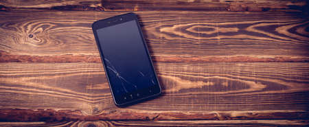 Black broken smartphone on a wooden background. Studio photo.の写真素材