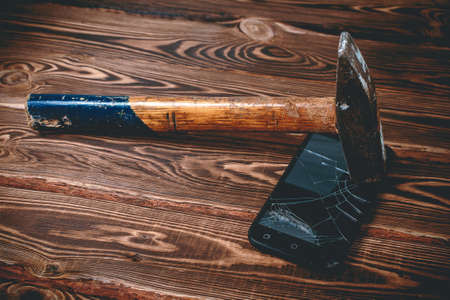 Old big hammer on a broken smartphone display. Studio photo on a wooden background.の写真素材