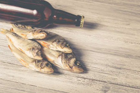 Dried perch and brown glass beer bottle on white wooden background. Studio photo.の写真素材