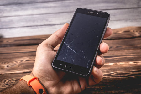 Broken black smartphone in hand on wood background. Studio photo for design