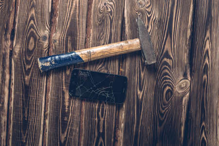 Old big hammer and broken smartphone on a wooden background. Studio photo.の写真素材