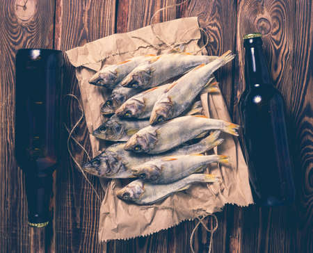 Beer bottles and dried fish on a paper bag on a wooden table. Studio photo.の写真素材