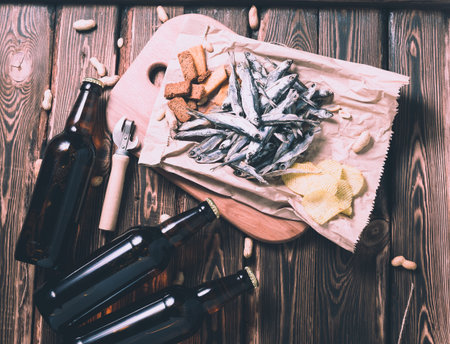 Brown glass bottles of beer and dried fish with chips, nuts, crackers on paper on a wooden background. Studio photo.の写真素材