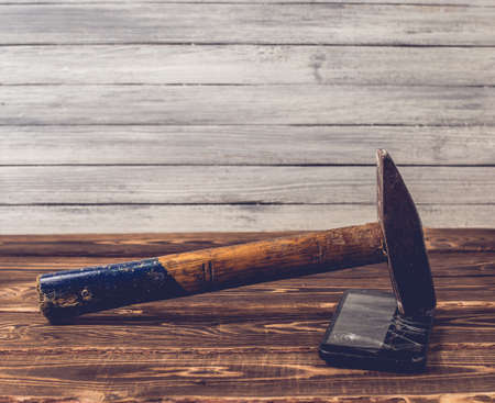 Old big hammer on a broken smartphone display. Studio photo on a wooden background.の写真素材