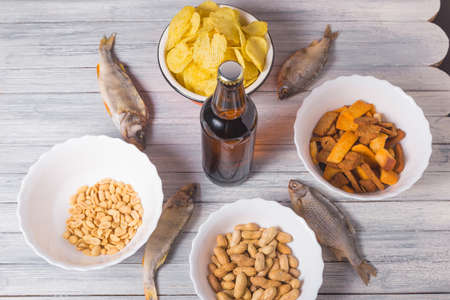 On a wooden table a bottle of beer, dried fish, chips, crackers and nuts. Studio photo.の写真素材