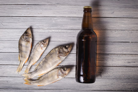 Dried perch and brown glass beer bottle on white wooden background. Studio photo.