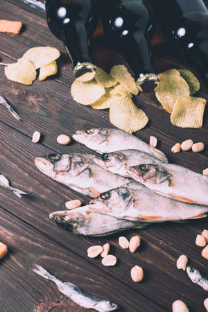 Dried fish, perch, bleak, chips, crackers, nuts and three brown glass bottles of beer on a wooden background. Studio photo.の写真素材