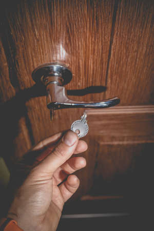 A man holds in his hand a small light broken key against the background of a door lock. Photo in the old style with vignetting.の写真素材