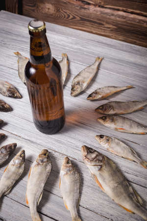 Dried perch and brown glass beer bottle on white wooden background. Studio photo.の写真素材